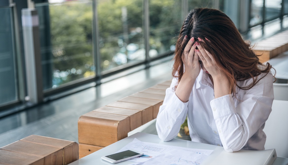 anxious female employee holding her head while working alone at a table