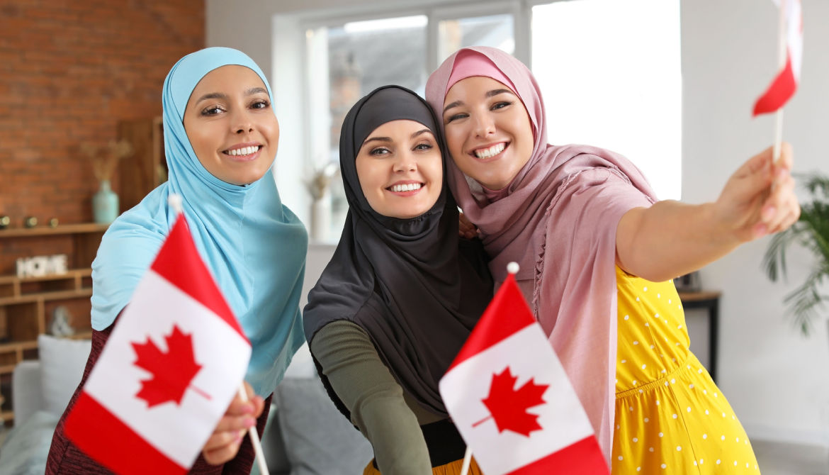 three young Muslim women in colorful headscarves wave Canadian flag