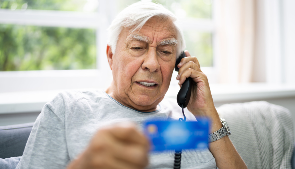 older man holds credit card while on the phone