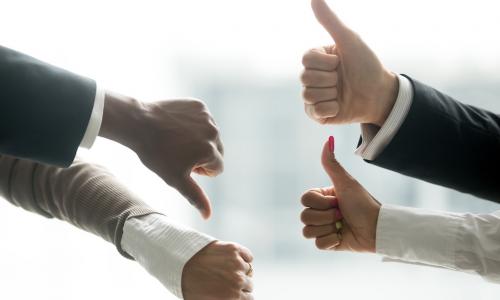 Hands of diverse business people showing two thumbs up and two thumbs down, suggesting equal opposing forces