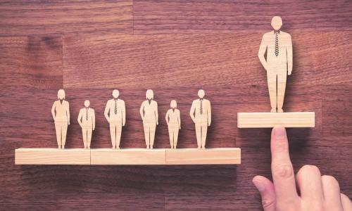 wooden figures in a row with a hand pushing one figure higher than the others