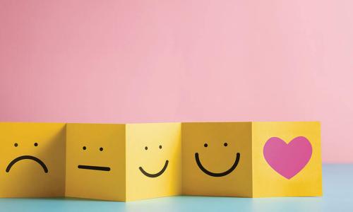 yellow strip of paper folded into boxes displaying smiley faces ranging from sad to happy and ending with a pink heart