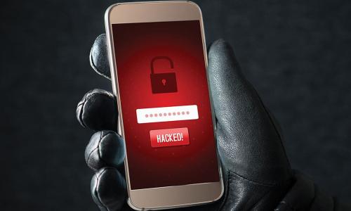 black leather gloved hand holds up smartphone with red screen depicting an open padlock and the word hacked