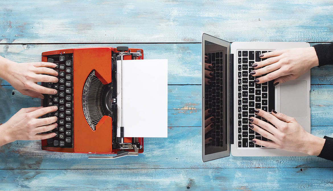 an old red typewriter across from a sleek new Mac laptop