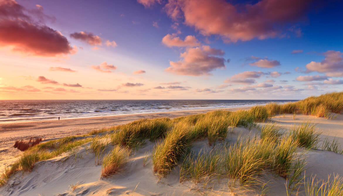 Seaside with sand dunes and colorful sky at sunset