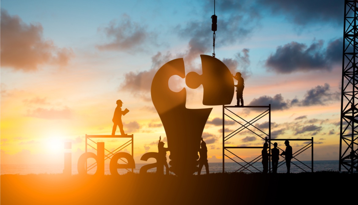 workers building a light bulb puzzle with a sunset behind