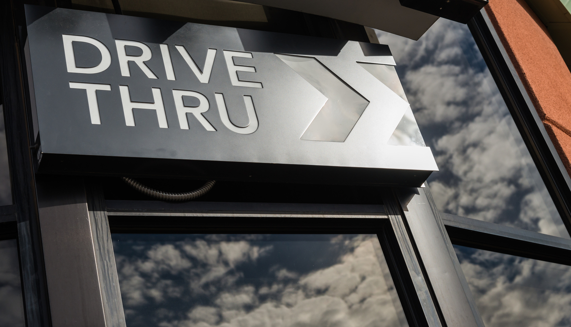 metal drive thru sign on a windowed exterior wall displaying reflection of clouds in the sky