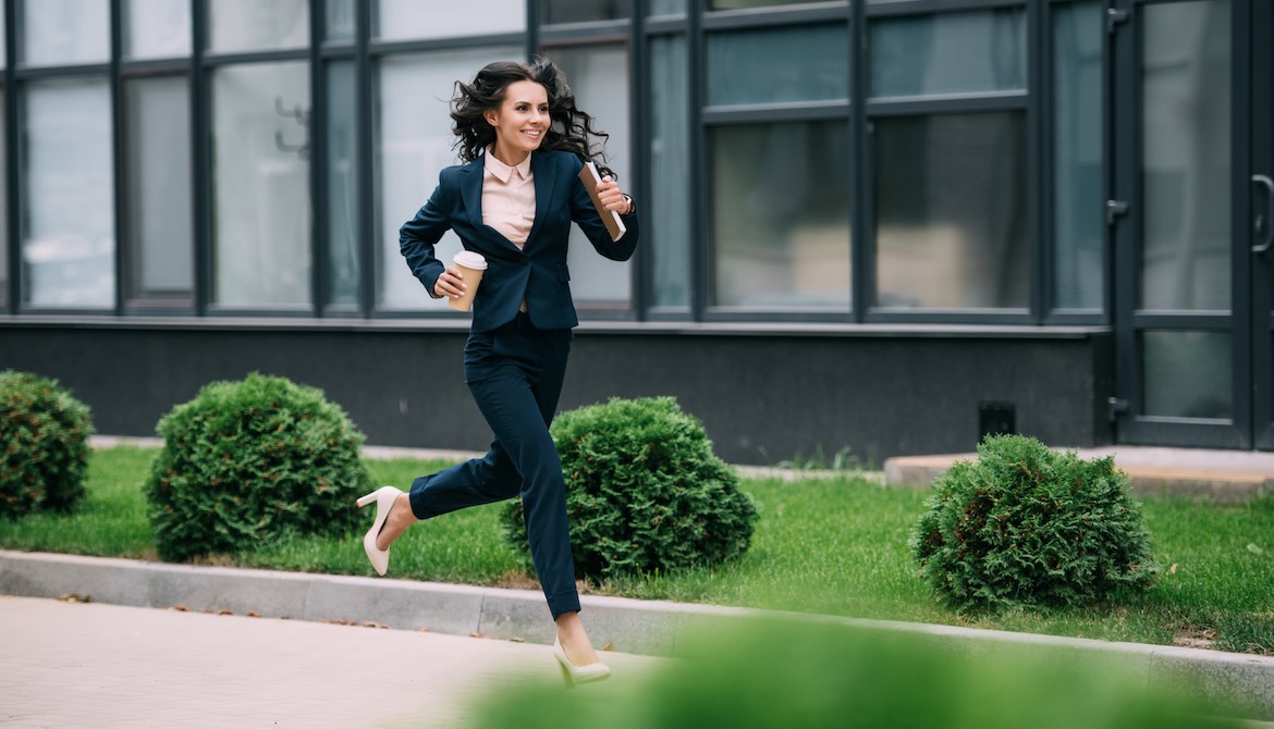 young happy businesswoman running to work in high heels with coffee and notebook