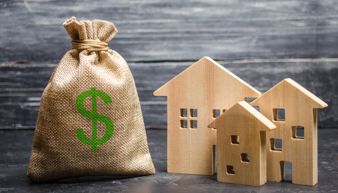 burlap bag with green dollar sign on it next to wooden houses