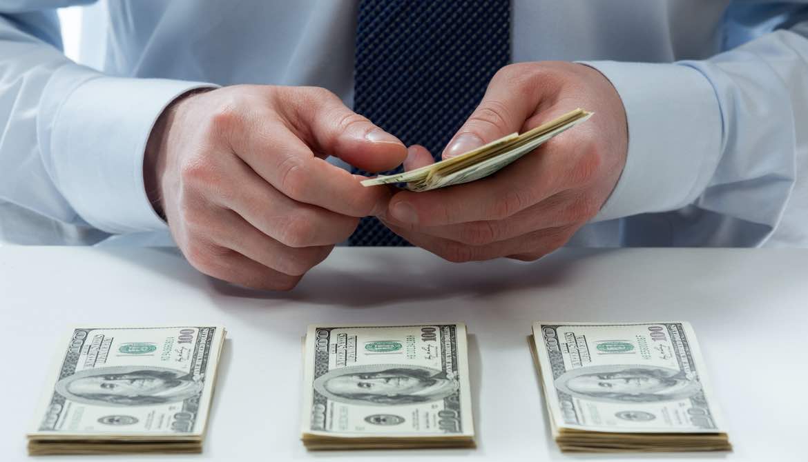 man's hands counting dollar banknotes on the table