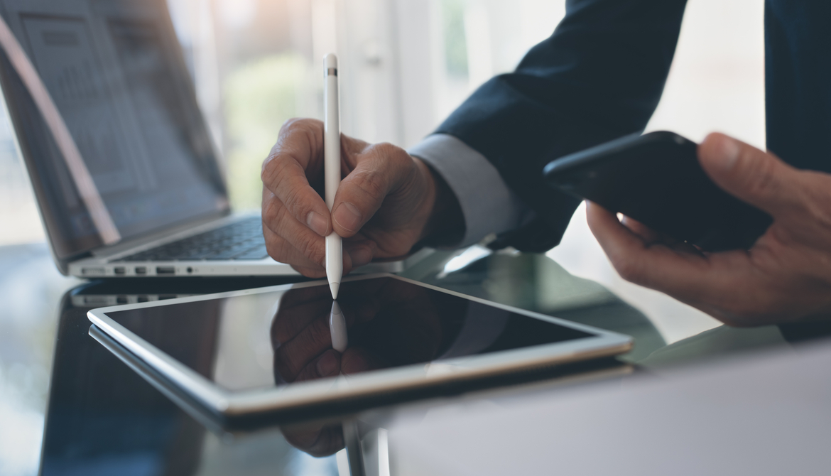 business man signing on tablet with laptop in background