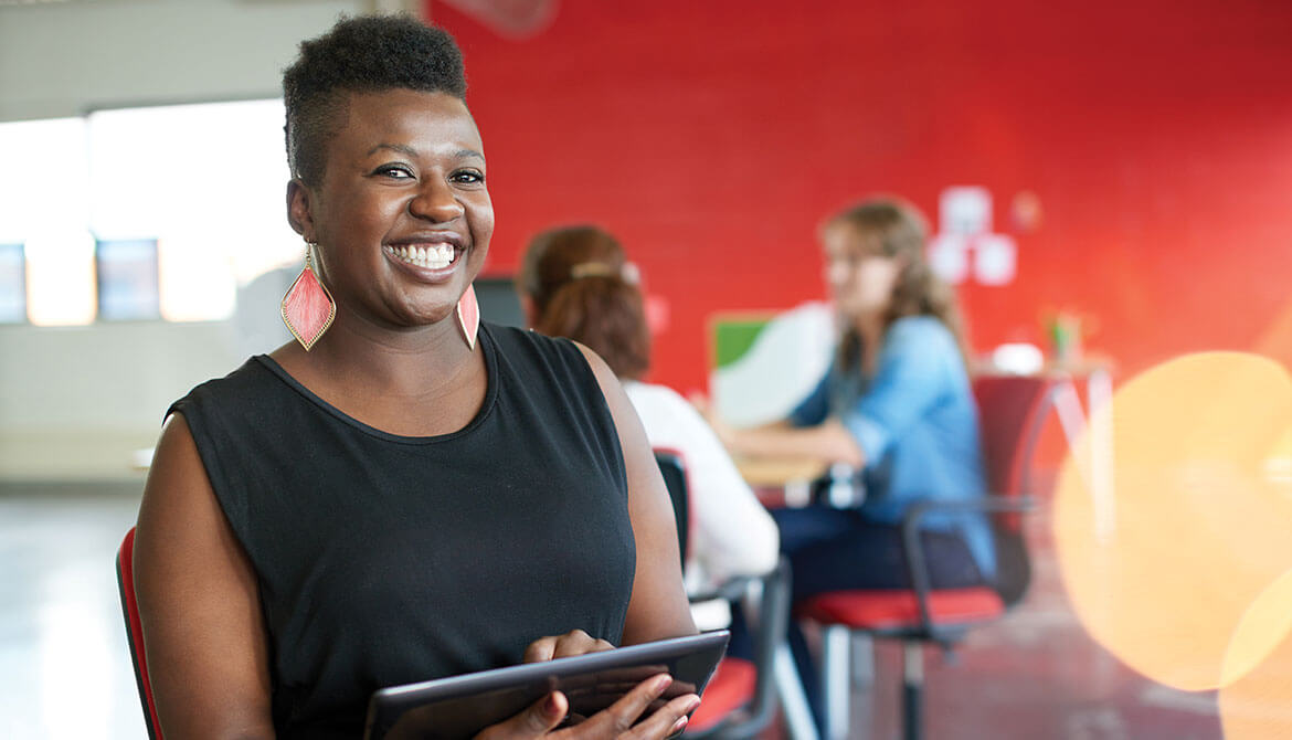 Smiling Black woman using tablet in busy workplace with bright red wall