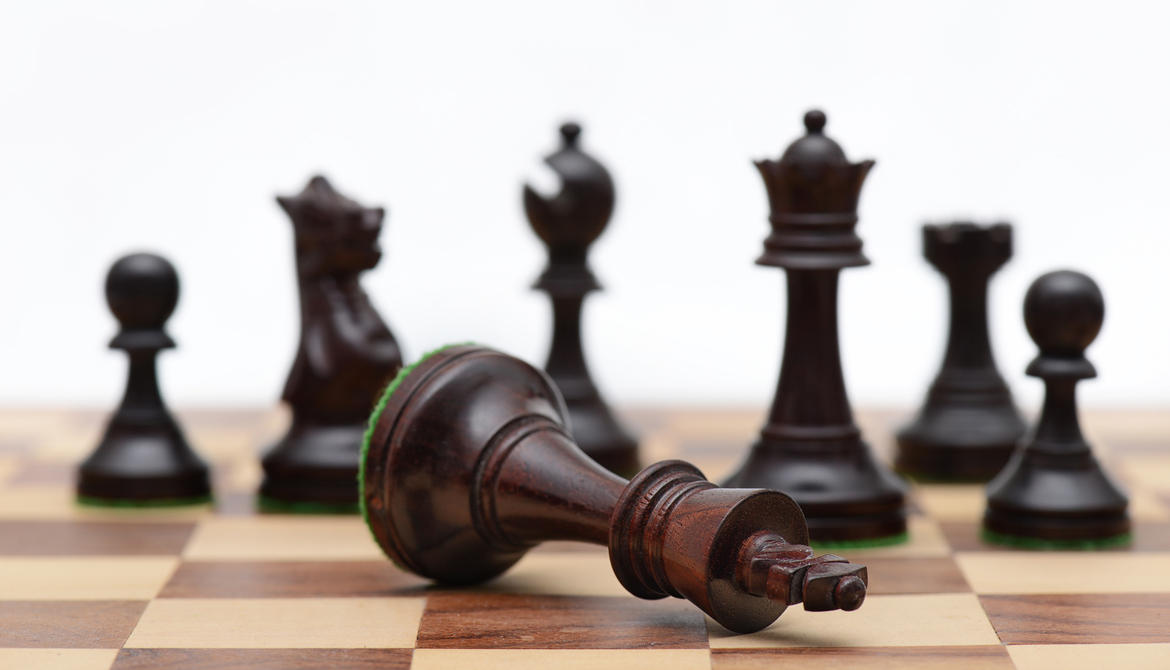 fallen black king chess piece in front of array of other black chess pieces