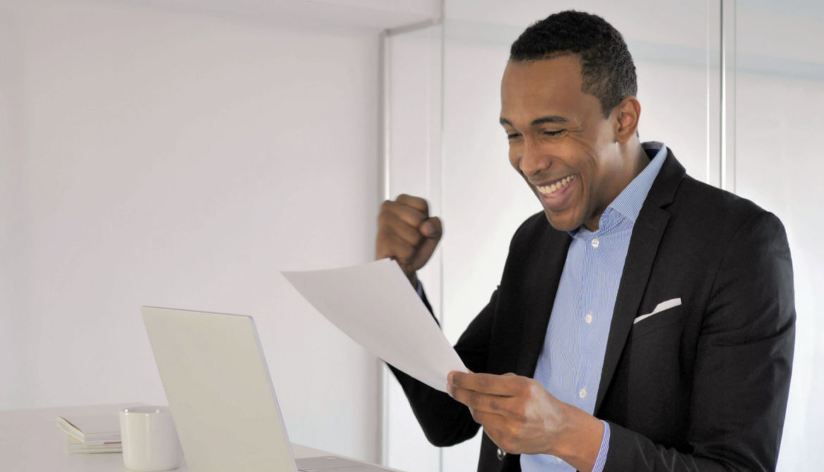 businessman celebrating with fist, laptop, paper