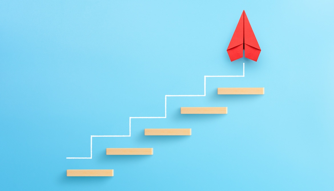 red paper airplane points upward as it progresses up wood block stairs