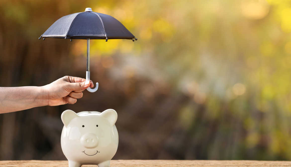 hand holds mini black umbrella over small piggy bank