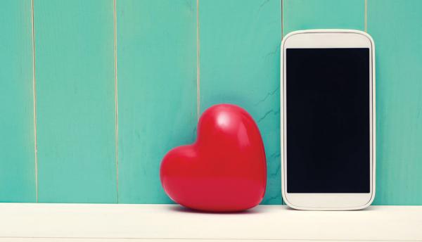 white smartphone next to shiny red heart in front of green wooden wall