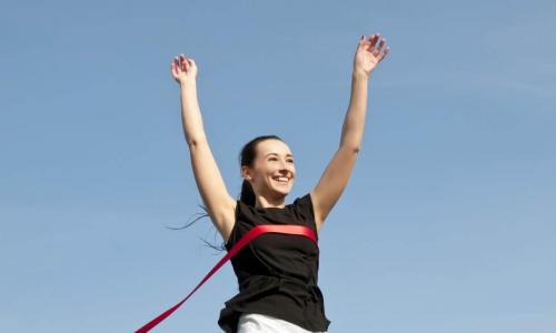 business woman breaks through tape at end of the race