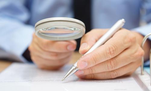 examiner reviewing paperwork in a binder through a magnifying glass representing due diligence