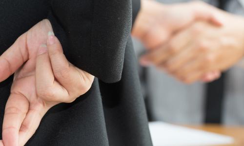 Businessman showing fingers crossed behind his back while he shakes hands