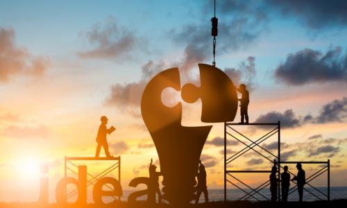 workers building a light bulb puzzle with a sunset behind