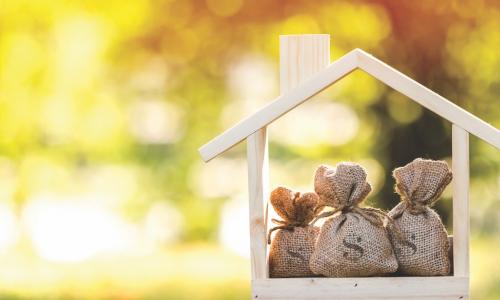 wooden house cut out with three bags of money inside