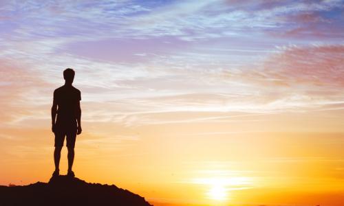 man standing on hill with sunset