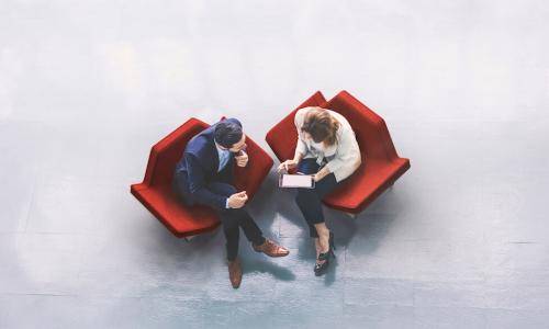 man and woman sitting in red chairs have a discussion