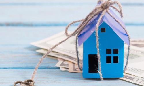 blue paper house tied to an old fashioned key sitting on a stack of US dollars