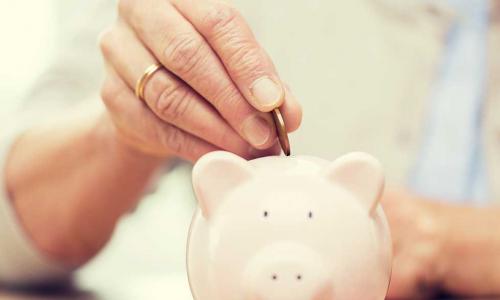 older woman’s hand putting a coin into a piggy bank