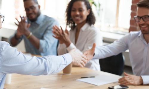 business professionals shaking hands in agreement while team applauds