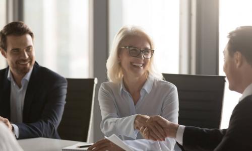 female director smiling and shaking hands with another board member