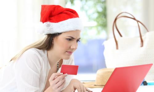 confused woman wearing a Santa hat using credit card with a red laptop