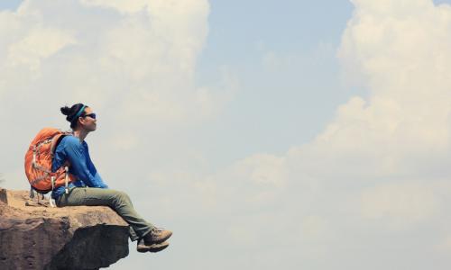 confident pensive hiker sitting on the edge of a cliff