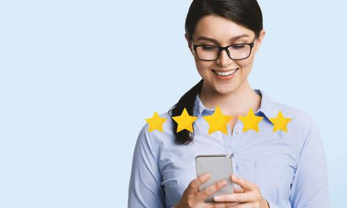 Smiling young woman wearing glasses using smartphone with five gold stars in foreground