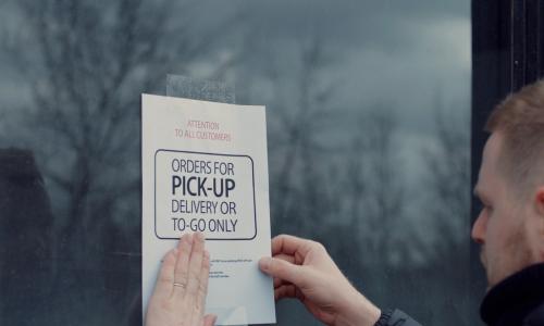 man putting up a take-out only sign on his closed restaurant business