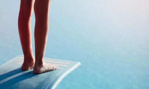 feet of person hesitating near edge of diving board above the water