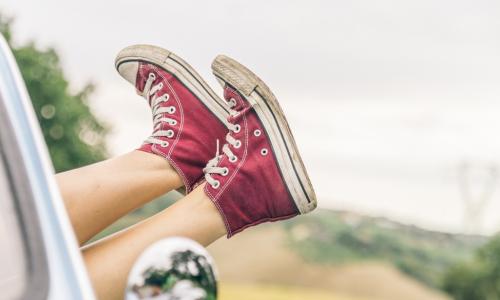 woman hanging feet in red sneakers out window of car