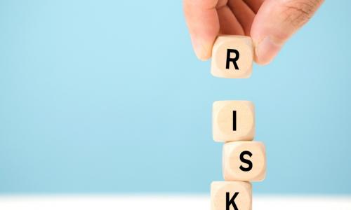 hand carefully placing R block on top of tower of letter blocks to complete the word RISK