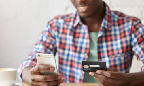 cheerful young African man using smartphone and credit card