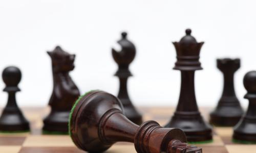 fallen black king chess piece in front of array of other black chess pieces